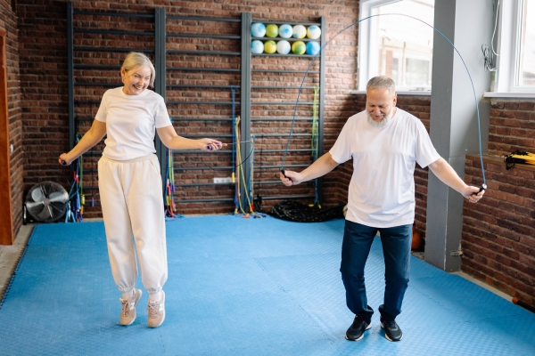 Ältere Frau und älterer Mann springen gemeinsam Seil in einem Trainingsraum und bewegen sich aktiv.
